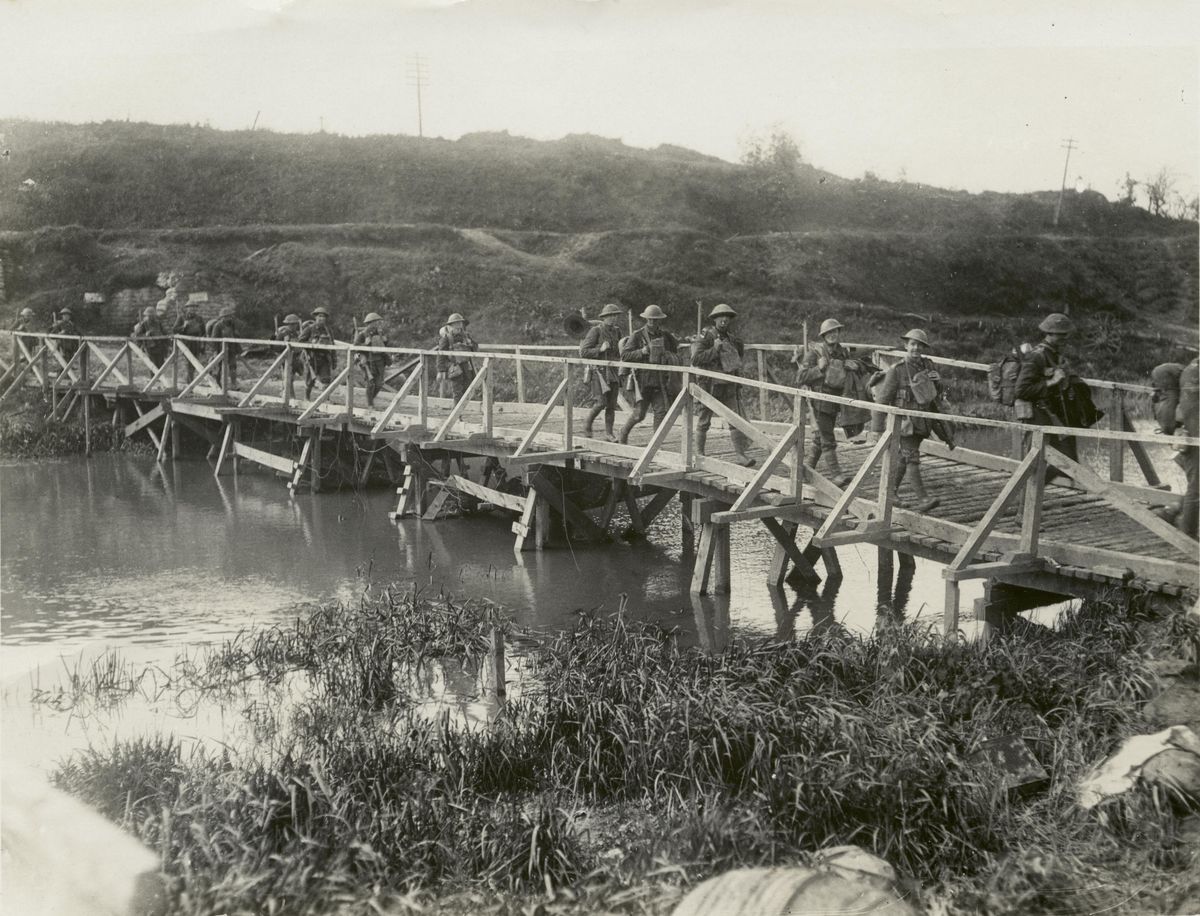 NZ soldiers cross a wooden bridge built by sappers near Ypres to replace crossings destroyed in battle (Henry Armitage)